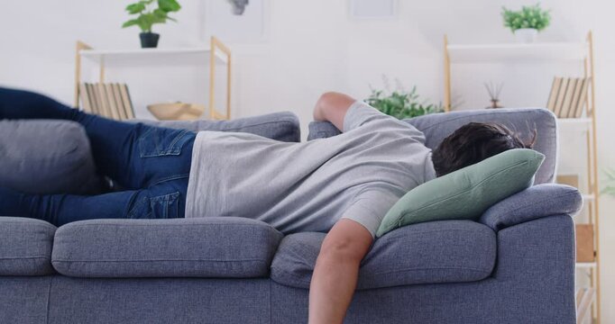 Very tired man comes home and falls face down on the sofa. Exhausted young man lies down on the couch to relax and have a nap. Fatigue, tiredness, stress, rest, relaxation concept