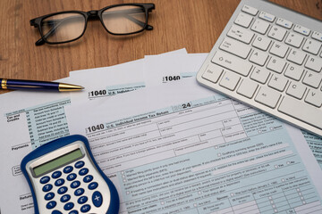 us individual 1040 tax forms with keyboard laptop calculator and other office supplies on desk.