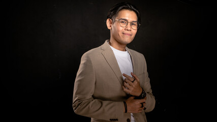 Asian man wearing beige blazer and white shirt standing in studio with dark background, confidently pointing to chest, ideal for branding, leadership, or creative business expression