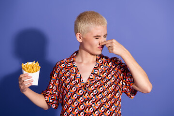 Stylish young woman holding a box of fries while expressing dislike on a bold pattern shirt with a...