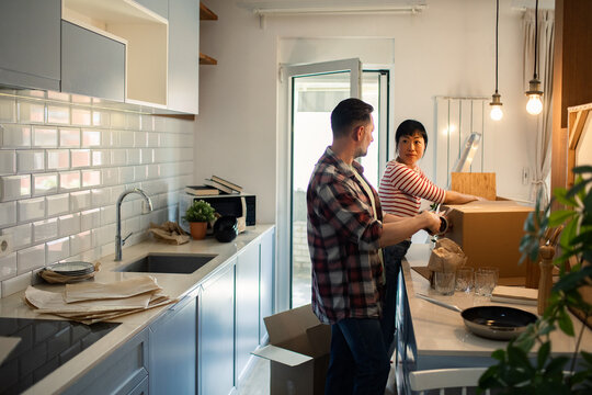 Happy couple unpacking kitchen items from moving boxes at home