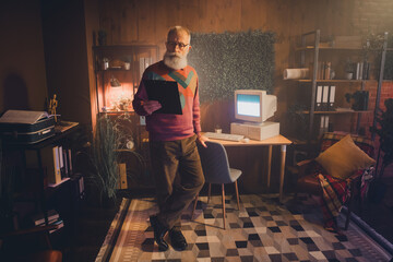 Elderly man in cozy office reading a clipboard next to a vintage desktop computer under warm...