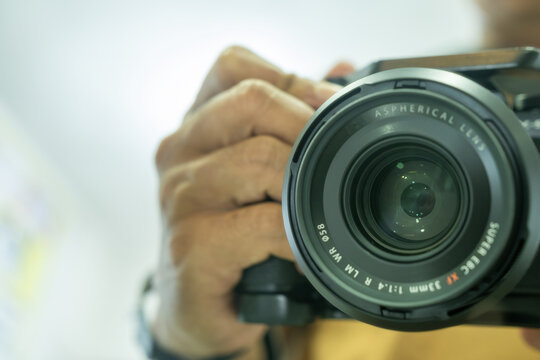 Close-up of photographer holding mirrorless camera, focus on aspherical lens text, creative workspace equipment, modern photography concept, clean bokeh background with soft natural lighting.