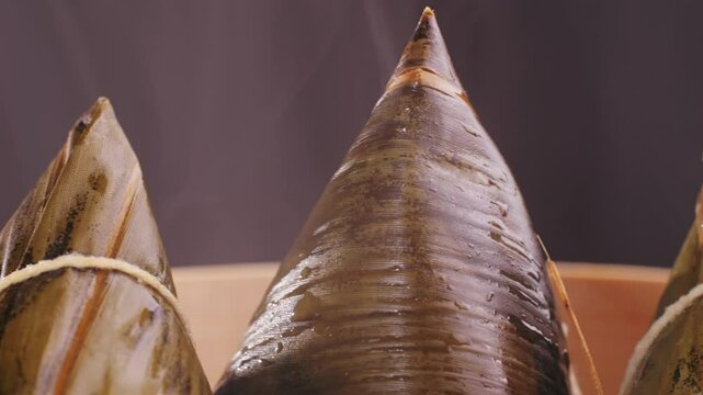 Hand holding zongzi (rice dumpling) with savoury fillings wrapped in bamboo or reed leaves.