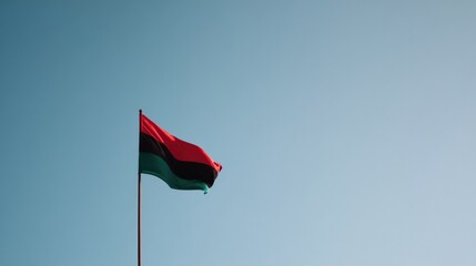 clean image of single red black and green flag against clear sky providing ample copy space