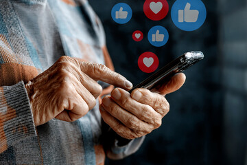  A close-up of elderly hands holding a smartphone, with red heart emojis floating above the device. The image depicts an older person using technology, symbolizing love, communication, and connection
