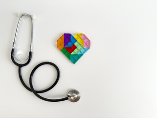 Stethoscope and colorful heart shape made of tiles on white background with copy space, showcasing the connection between health and care