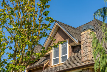 Top of grey stucco luxury house with shingle roof, green trees and nice windows in Spring in Vancouver, Canada, North America. Day time on April 2025.