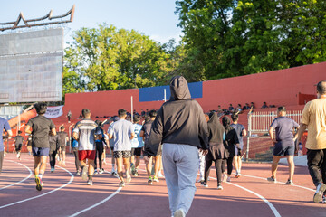 A crowd of individuals actively jogging together on a track in a large outdoor stadium.