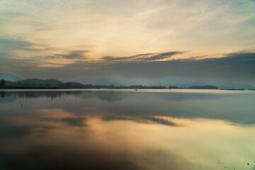 Sunset reflecting on calm lake with mountains and cloudy sky