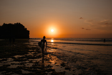 Fototapeta premium Silhouette of a surfer on the ocean shore against the sunset