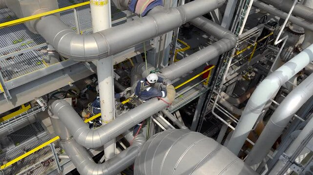 Aerial high angle shot of technicians repairing a plant in an oil or chemical refinery. Industrial rope access workers descending to grind and repair a turbine. Working at height. Rappelling, Abseilin
