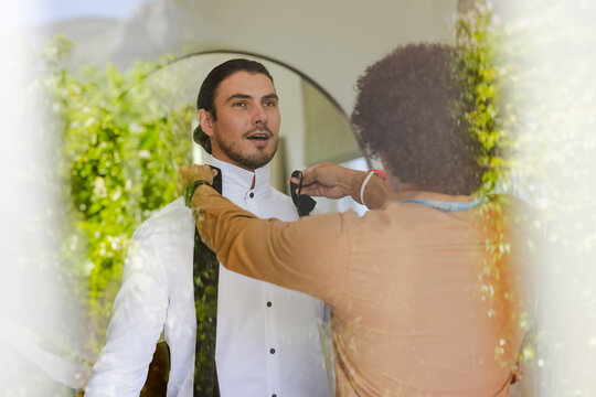 Wedding suits, stylist and client adjusting collar in fitting room, with mirror