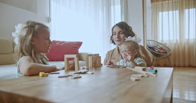A mother and her two young daughters enjoy quality time together while playing with wooden blocks at home.