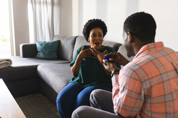 Proposing African American couple kneeling beside sofa at home, showing ring box
