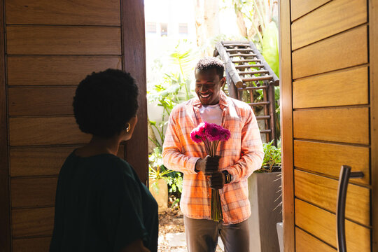 African American couple standing at wooden front entryway, holding pink bouquet with waterwheel