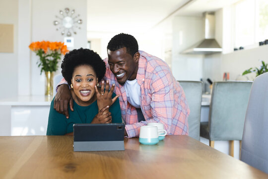 Couple showing engagement ring on video call in modern home kitchen, with laptop