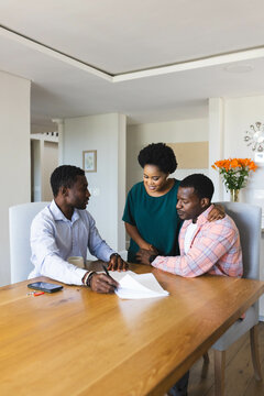 Reviewing financial paperwork African American couple with advisor at dining table, with coffee mug