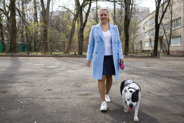 A woman in a blue coat walks a black and white dog on a leash