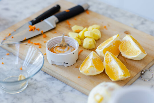 Wooden cutting board showing orange wedges, cubes and juicer with knife on marble counter