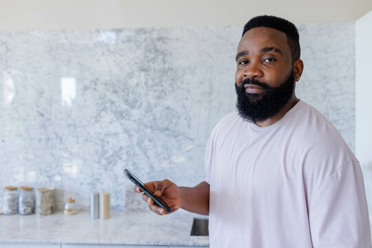African American man using smartphone in home kitchen, with canisters, copy space