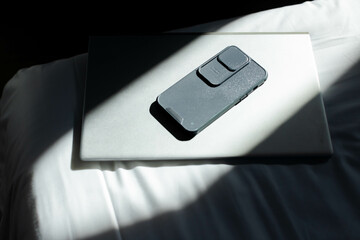 Black smartphone resting on silver laptop on white bed, highlighting magnetic case attachments