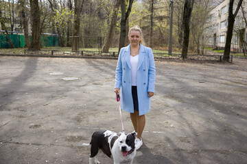 A woman in a blue coat walks a black and white dog on a leash