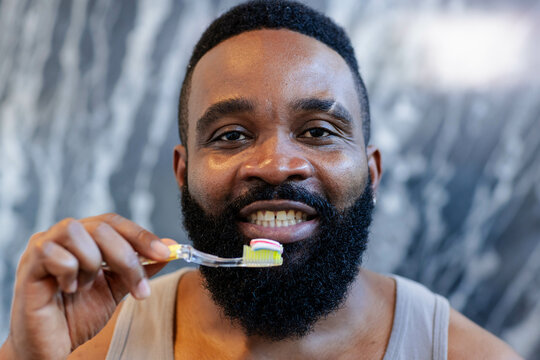 African American man brushing teeth in bathroom, with toothbrush and colorful toothpaste