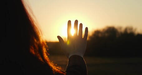 female silhouette sunset stretches out her hand to sun, personifying sustainability and care for...