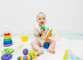 A 5-7 month old baby sits on the floor and plays with bright toys in his room.