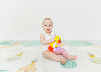 A 5-7 month old baby sits on the floor and plays with bright toys in his room.