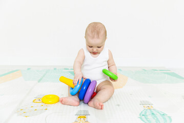A 5-7 month old baby sits on the floor and plays with bright toys in his room.