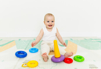 A 5-7 month old baby sits on the floor and plays with bright toys in his room.
