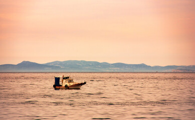 Fototapeta premium A very small fishing boat on a grey and calm sea and under a red sky. Beautiful dusk view in evening.