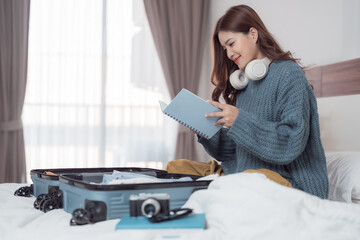 Young tourist reading a travel journal while packing luggage on the bed in a hotel room, eagerly preparing for an upcoming vacation filled with excitement and adventure