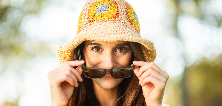 Playful woman lifting sunglasses while wearing a crochet hat