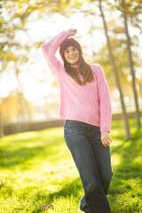 Smiling woman in pink sweater and jeans posing in a sunlit park
