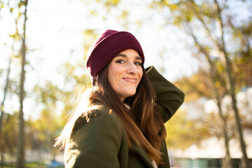 Portrait of a young woman in a beanie and green coat smiling confidently in an autumn park