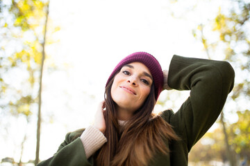 Close-up portrait of a smiling woman in a beanie and green coat in a sunny park