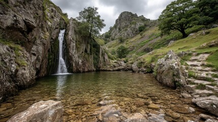 Obraz premium Serene waterfall cascading into a clear pool, nestled amongst rocky hills under a cloudy sky. Tranquil landscape photography.