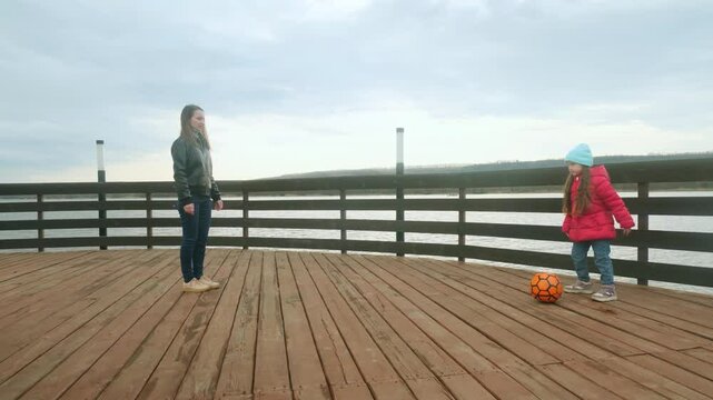 Mother and daughter at the pier near the water having fun. Mom with little girl playing a ball