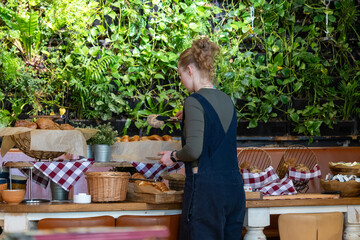 A woman in a blue apron is standing in front of a table full of food on breakfast