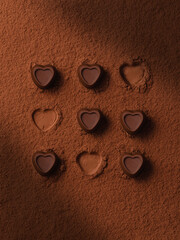 Chocolate candies heart on the cocoa powder background. Still life of chocolate hearts with aesthetic sunlight shadows. Valentines day concept