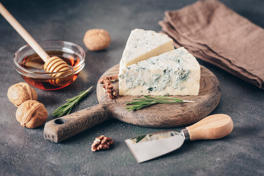 Blue cheese with honey, walnut, rosemary and cheese knife, dark rustic background, selective focus