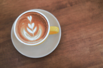 Close-up of hot cappuccino with beautiful latte art in yellow ceramic cup on wooden table.
