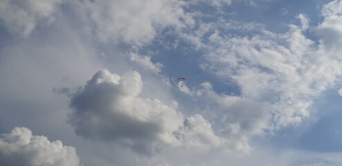 Clouds form a stunning backdrop as a parachutist descends through the open sky during an afternoon adventure