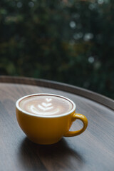 Close-up of hot cappuccino with beautiful latte art in yellow ceramic cup on wooden table.
