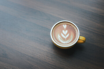 Close-up of hot cappuccino with beautiful latte art in yellow ceramic cup on wooden table.
