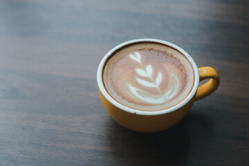 Close-up of hot cappuccino with beautiful latte art in yellow ceramic cup on wooden table.
