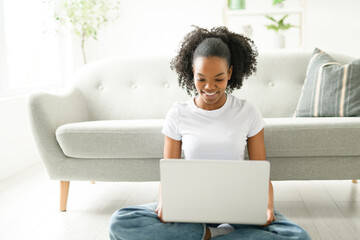 Young woman sitting on floor by the couch using laptop. Afemale working on laptop computer at home.